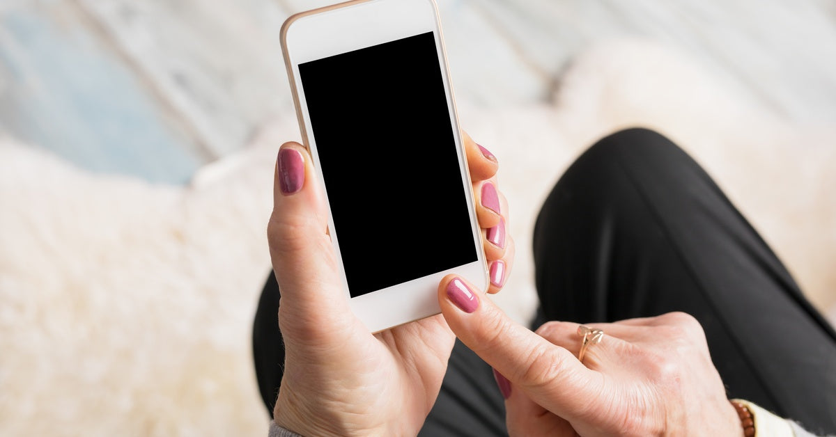 Someone holds a smaller smartphone with a black screen. Their pointer finger touches something on the screen.