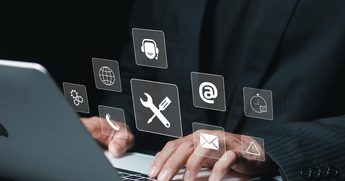 A person in a dark suit types on a laptop. Digital service icons including tools, cloud, and support, float above the keyboard.