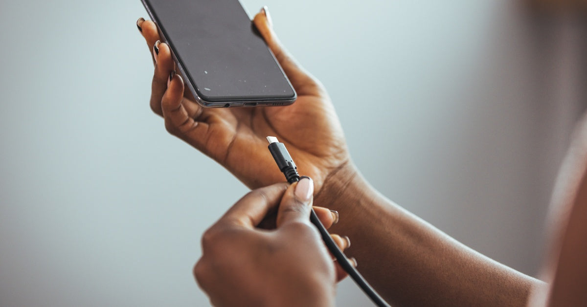 Someone holds a smartphone in their hand and a charging cable in the other. They hold up the cable to the bottom of the phone.